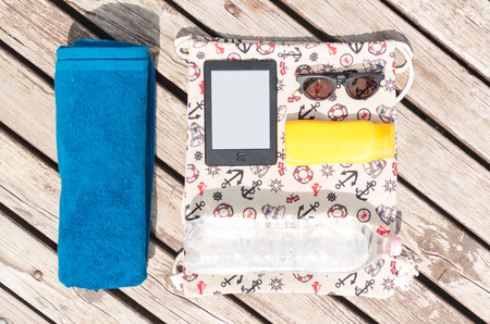 Organized beach pack with towel, sunglasses, ebook reader, suncream and drinking water on a bagの写真素材