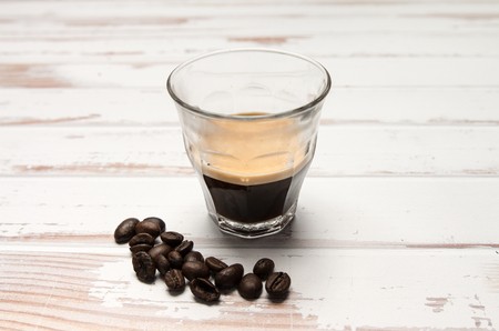 Fresh espresso with crema on a white table with some coffee beansの写真素材