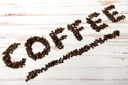The word coffee written with fresh coffee beans on a white wooden tableの写真素材