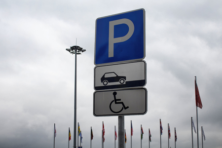 Car park sign for disabled people with nations' flags on poles in the background in Moscow. It is cloudy day in autumun.の写真素材