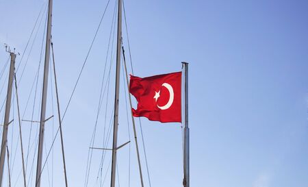 Turkish flag waves with clear blue sky and masts of yachts at marina in Bodrum.