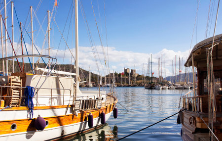 View of wooden yachts parked at Bodrum marina and famous castle landmark in a calm autumn day.のeditorial素材