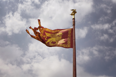 View of historical Venetian flag waving with cloudy sky background.の写真素材