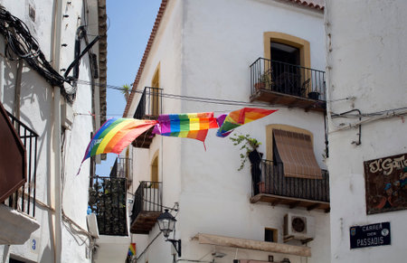 View of Gay flags waving with historical, traditional white buildings in the background in Ibiza. It is Calle de la Virgen streetのeditorial素材