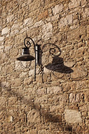 Decorative black street lamp (lantern) and its shadow on historical stone wall in Cunda (Alibey) island.の写真素材