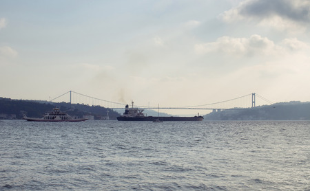 Dry cargo vessel and car ferry pass Bosphorus in Istanbul. FSM bridge is in the background.