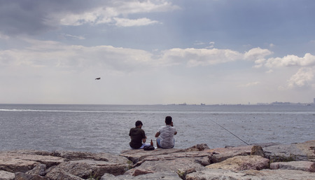 View of two young unrecognizable men sitting on the rocks by Bosphorus. Image is captured in the neighborhood called Moda located on the Asian side of Istanbul.の写真素材