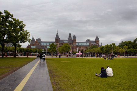 View of people at hanging out at Museum Quarter (square) in Amsterdam. Rijksmuseum is in the view. It is a summer day with cloudy sky.のeditorial素材