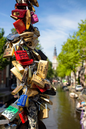 Close up view of wish/love locks (lovers padlocks) with canal, trees and Zuiderkerk church in the background in Amsterdam. It is a sunny summer day.のeditorial素材