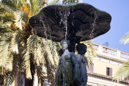 View of historical water fountain and palm trees at famous city square called "Placa Reial" in Barcelona. It is a sunny summer day.のeditorial素材