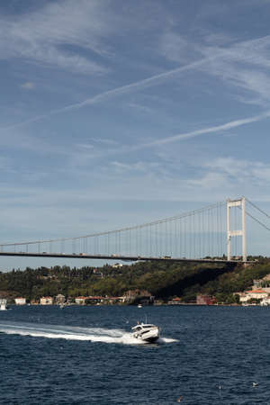 View of a yacht passing on Bosphorus and FSM bridge in Istanbul. It is a sunny summer day. Beautiful travel scene.の写真素材