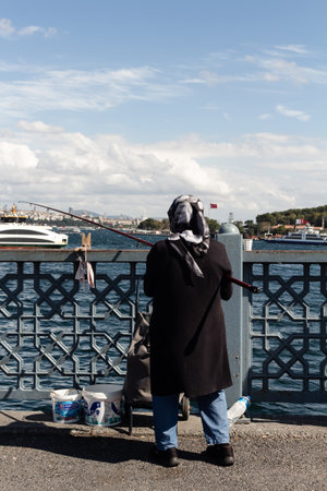 View of unrecognizable fisherwoman on Galata bridge in Istanbul. The image reflects lifestyle and culture of local people It is a sunny summer day.のeditorial素材