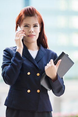asian Businesswoman talking on the phone and holding document file.の写真素材
