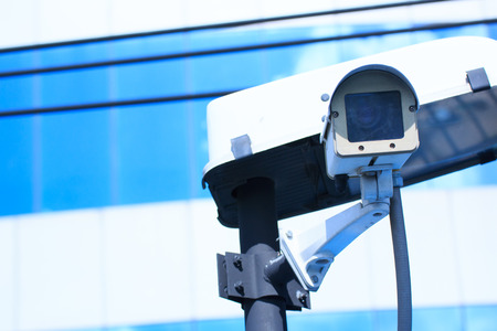 Camera system guarding blue skyscraper office building with sky above