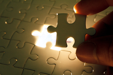 Hand insert missing jigsaw puzzle piece with light glow, business concept for completing the final puzzle pieceの写真素材