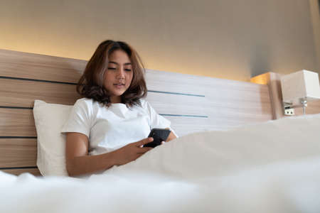 Young asian women lying in bed texting and checking social apps in smartphone on bed before after she sleeping at night. Mobile addict concept.の写真素材