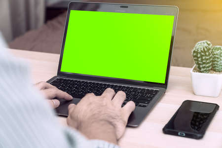 Young businessman in eyewear  working at home with laptop and phone on desk. Pleasant happy man communicating in social network, searching information online.の写真素材
