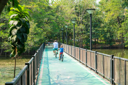 Children and adults relax and happy riding on bikes in the park near city and Building.の写真素材