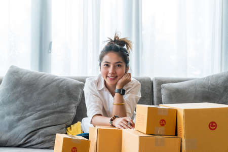 Beautiful Asian women sitting on sofa with many parcel box with small businesses sell to customer on shopping online. Concept selling and shopping online from homeの写真素材