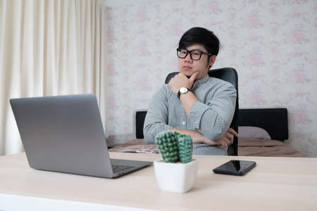 Young businessman in eyewear  working at home with laptop and phone on desk. Pleasant happy man communicating in social network, searching information online.の写真素材