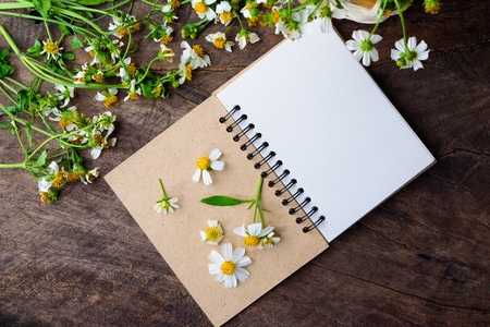 Blank notebook with white flower and bas ket of flower on vintage wooden table View from above with copy spaceの写真素材