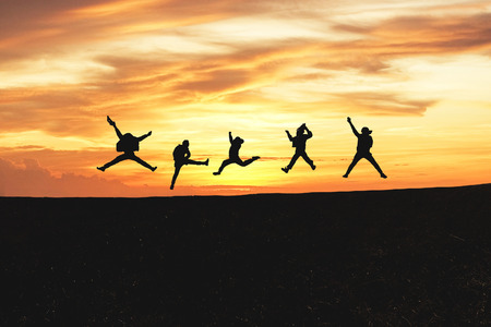 Concept of emotion. Silhouette of a happy group of people jumping at sunset in the mountain with copy space.の写真素材