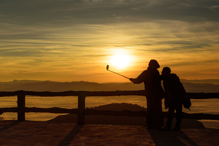 silhouette style of couple on the top of view point in the mountain while selfie during sunrise and sea of fog or mistの写真素材