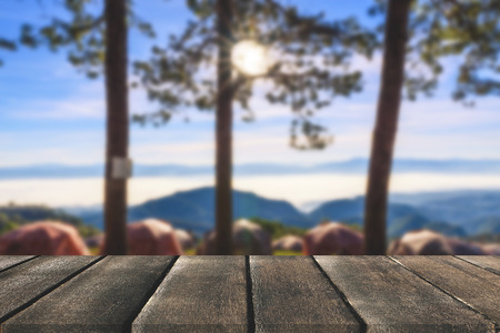 Wooden board empty table in front of tree background. Perspective brown wood over tent and pine tree...