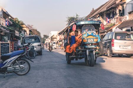 LUANG PRABANG, LAOS - February 16, 2017: Driver in parked tuk-tuk on while carrying young monk in the morning at  Luang Prabang.のeditorial素材