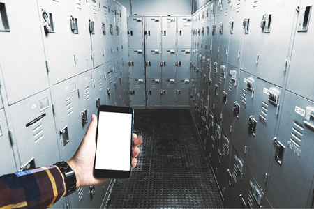 Hand in hipster shirt holding blank smartphone with locker in gym  background for mocup your product display.の写真素材