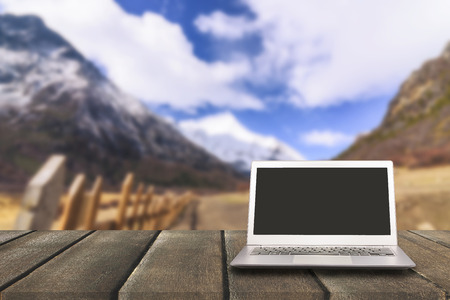 Laptop with blank screen on wooden table with forest in mountain and pine trees background, can used for display or montage your productsのeditorial素材
