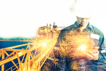 Double exposure of Engineer or Technician man with safety helmet operated platform or plant by using tablet with offshore oil and gas platform background for oil and gas business conceptの写真素材