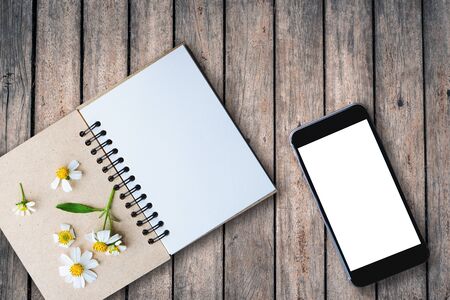 top view image of open notebook with blank pages next to chamomile flower, blank smart phone on old wooden table. ready for adding text or mockupの写真素材