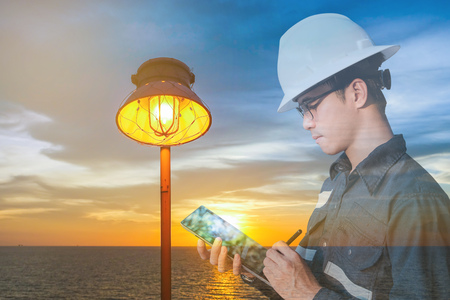 Double exposure of  Engineer or Technician man in working shirt  working with tablet in lamp and sea...