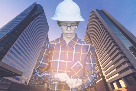 Double exposure of  Engineer or Architecture woman in hipster shirt and safety helmet working with tablet in night building background , business and construction concept.の写真素材