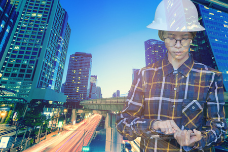 Double exposure of  Engineer or Architecture women in working shirt and safety helmet working with tablet in night building background , business and construction concept.の写真素材