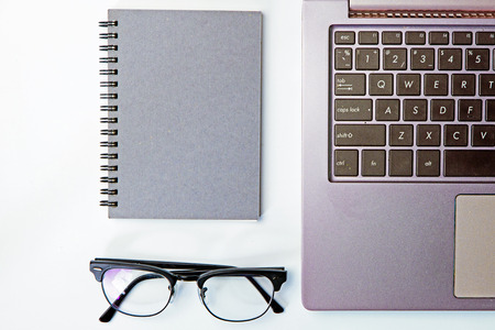 Top view of business working place with notepad,modern glasses,keyboard on white table,flatlay concept.の写真素材