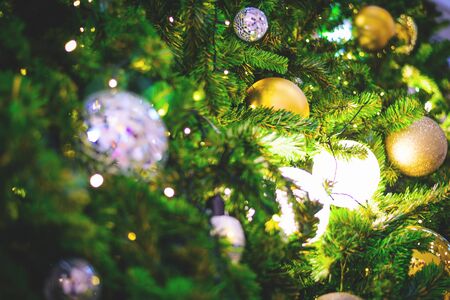 Closeup and selective focus of golden and silver bauble hanging from a decorated Christmas tree with...