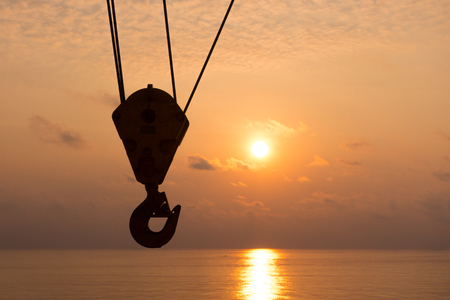 crane hook silhouette in sunset time with sea background in offshore oil and gas platform for heavy industry concept.の写真素材