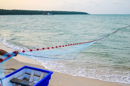 Close view of some blue fishing net floaters on the beach with boat and human while laying nets on...