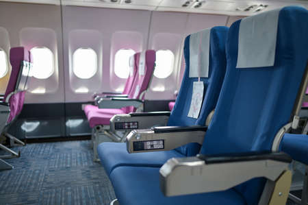 Empty passenger airplane seats in the cabin blue and pink with social distancing to prevent covid19 infection during pandemic.の写真素材