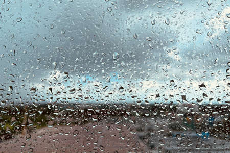 Rain drops on the clear glass. Beautiful raining sky with city background.の写真素材