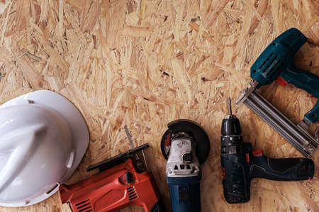 Group of electric hand tools jigsaw, grinder, drill, nail gun and white safety helmet on wooden background.の写真素材