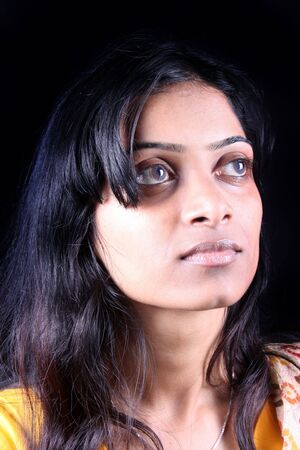 A portrait of a beautiful daydreaming Indian girl, on a black studio background.の写真素材