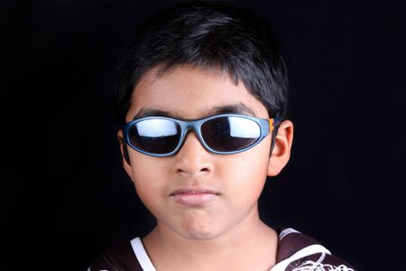 A portrait of a stylish Indian kid wearing sunglasses, on a black studio background.
