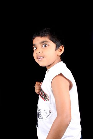A portrait of a cute Indian boy showing his fist telling that he is ready for fight, on black studio...