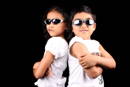 A portrait of two stylish Indian kids posing back to back making faces, on a black background.の写真素材