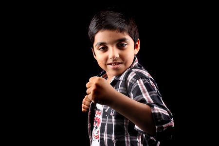 A portrait of a cute Indian boy showing his fist telling that he is ready for fight, on black studio background. Focus on the fist.の写真素材