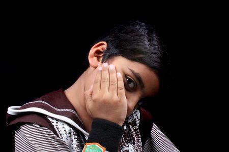 A portrait of a shy Indian boy, on black studio background.の写真素材