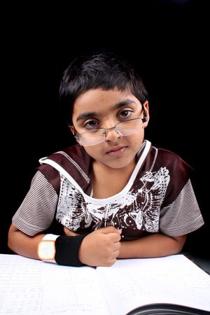 A genius but tired Indian kid doing his homework , on black studio background.の写真素材